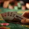 Person holding a fan of playing cards over a poker table surface in a casino setting.